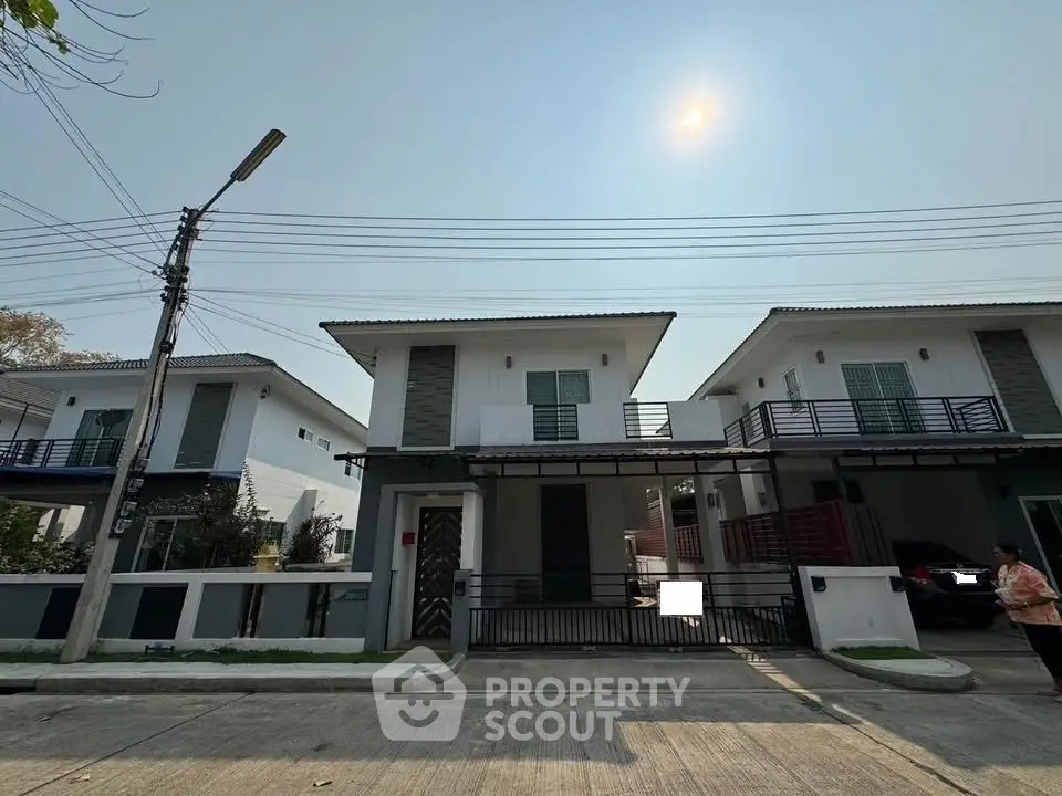 Modern two-story houses with balconies and gated driveways under a clear sky.
