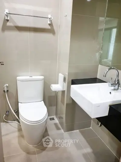 Modern bathroom with sleek fixtures and neutral tiles, featuring a toilet and a stylish sink.