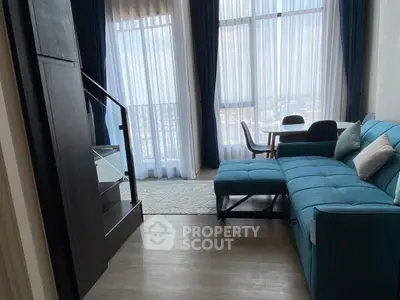 Modern living room with blue sectional sofa and large windows offering city views.