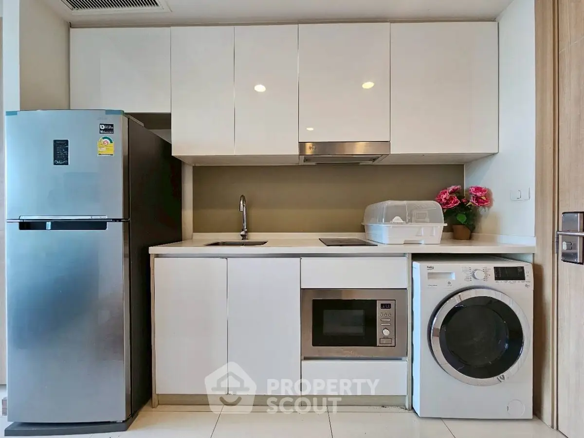 Modern compact kitchen with appliances including fridge, microwave, and washing machine.