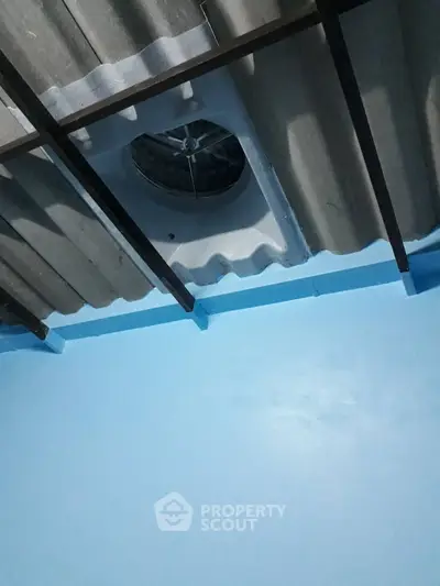 Ceiling with corrugated metal roof and ventilation fan in a blue-painted room.