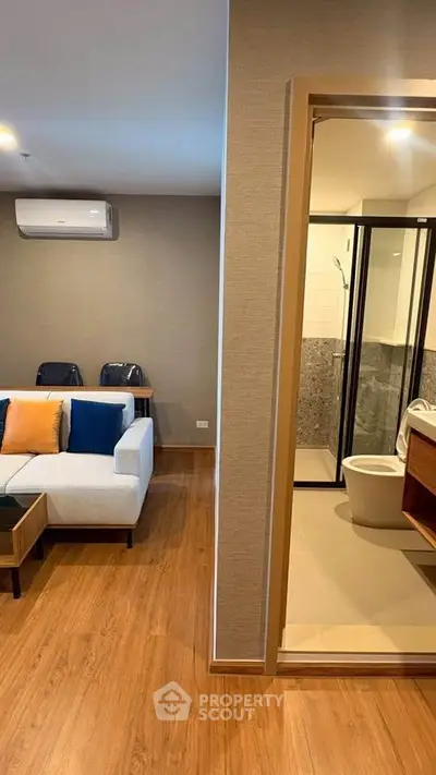 Modern apartment interior with cozy living room and adjacent bathroom, featuring stylish decor and wooden flooring.