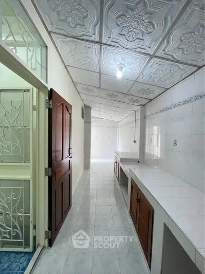 Spacious kitchen with tiled countertops and decorative ceiling tiles in a bright, airy layout.