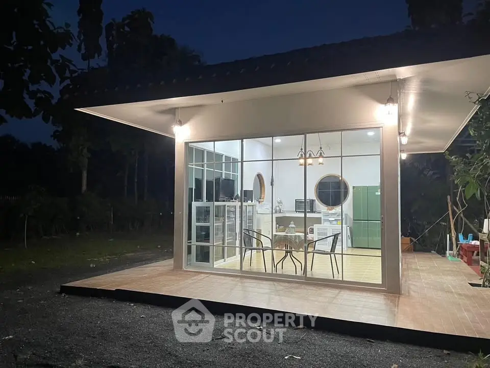 Modern glass-walled home with outdoor patio and stylish interior lighting, perfect for serene living.