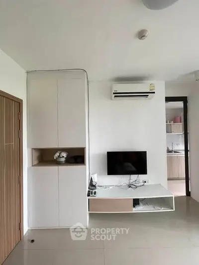 Modern living room with sleek TV setup and built-in storage, featuring minimalist design and air conditioning.