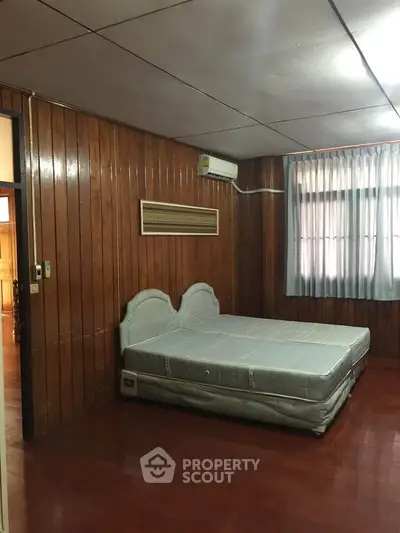 Cozy bedroom with wooden paneling and natural light, featuring a comfortable bed and air conditioning.