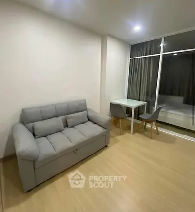 Modern living room with gray sofa and dining table, featuring large window.