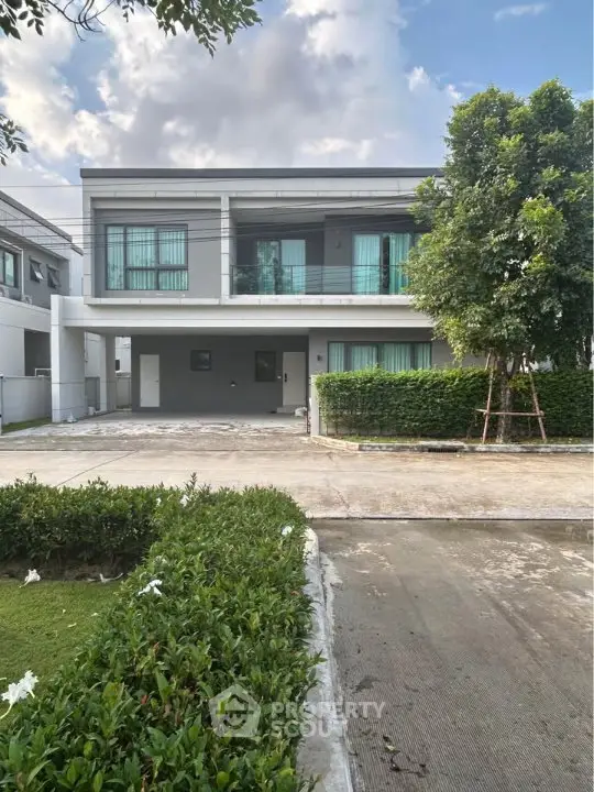 Modern two-story house with large windows and lush greenery in a serene neighborhood.