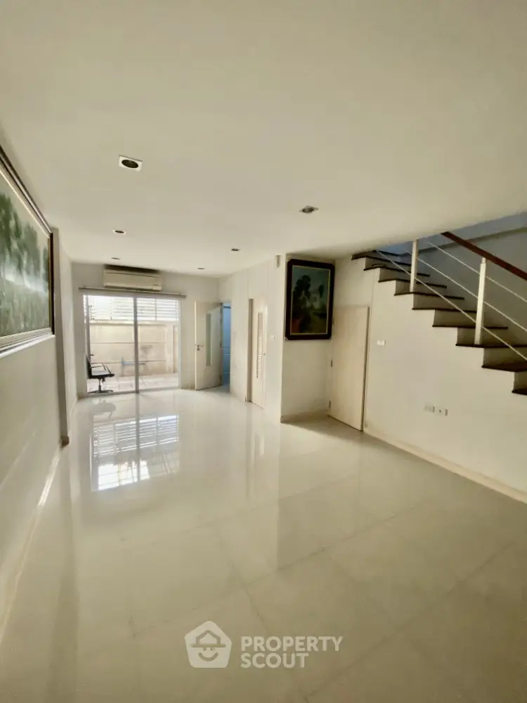 Spacious modern living room with sleek staircase and large window for natural light.