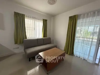 Bright living room with modern sofa and wooden coffee table, featuring large windows and green curtains.