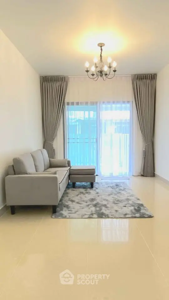 Spacious living room with elegant chandelier and modern gray sofa set.