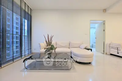 Modern living room with sleek white sofa and glass coffee table, featuring floor-to-ceiling windows.