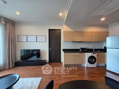 Modern open-plan living room with kitchen, featuring wooden flooring and sleek appliances.
