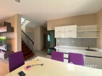 Modern kitchen with sleek design and open layout, featuring purple chairs and a staircase view.