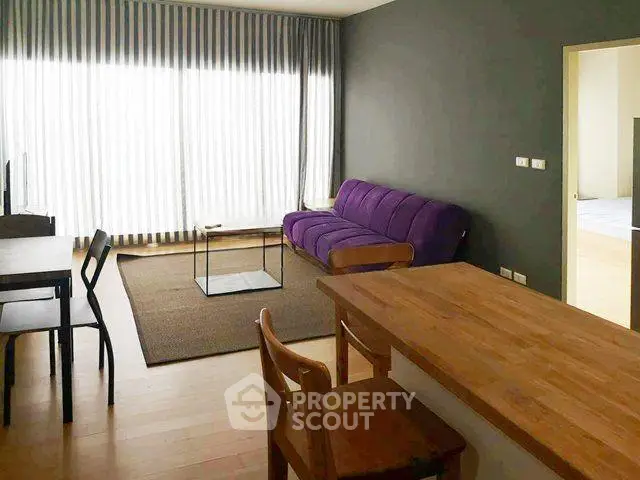 Modern living room with purple sofa and wooden dining table in bright apartment.
