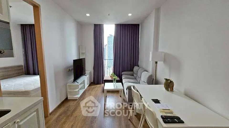 Modern living room with city view, featuring cozy sofa, TV, and dining area in open layout apartment.