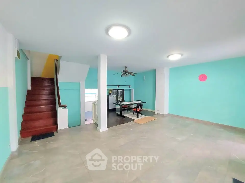 Spacious open-plan living area with modern staircase and vibrant teal walls