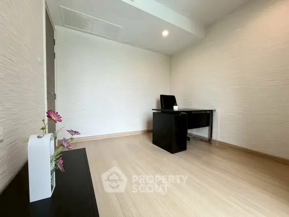Modern minimalist study room with sleek desk and chair, light wood flooring, and decorative flowers.