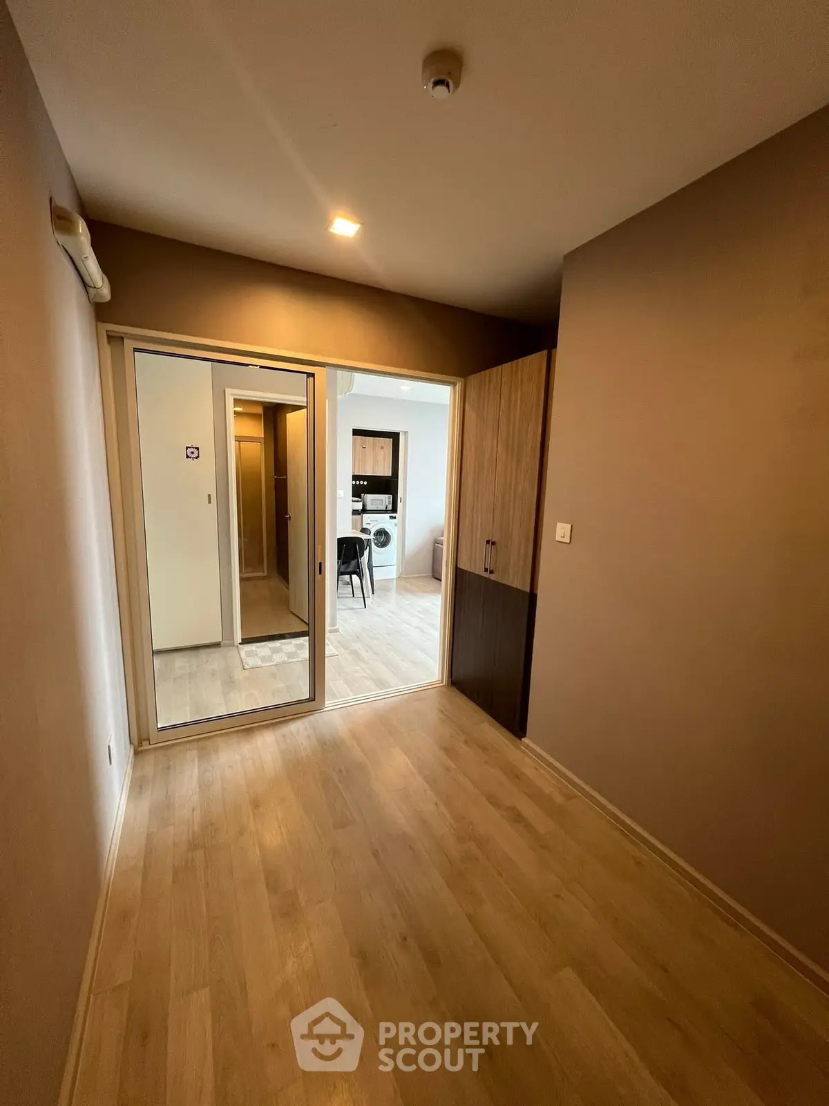 Spacious room with wooden flooring and sliding glass doors leading to a modern kitchen.