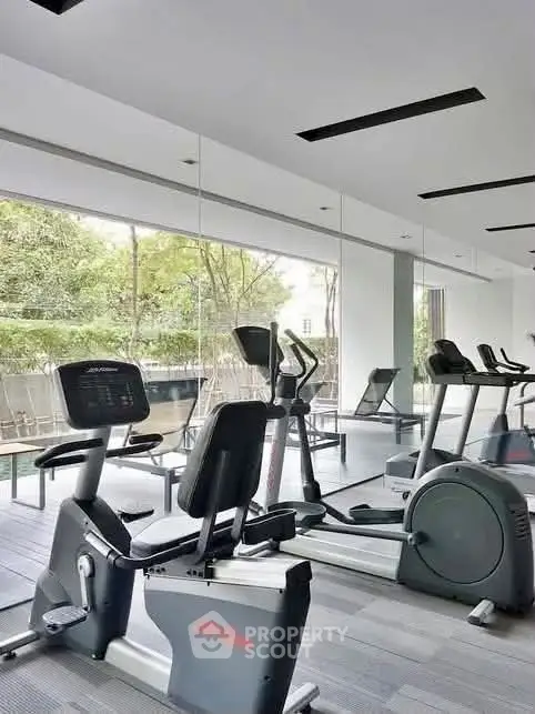 Modern gym with exercise equipment and large windows overlooking greenery.