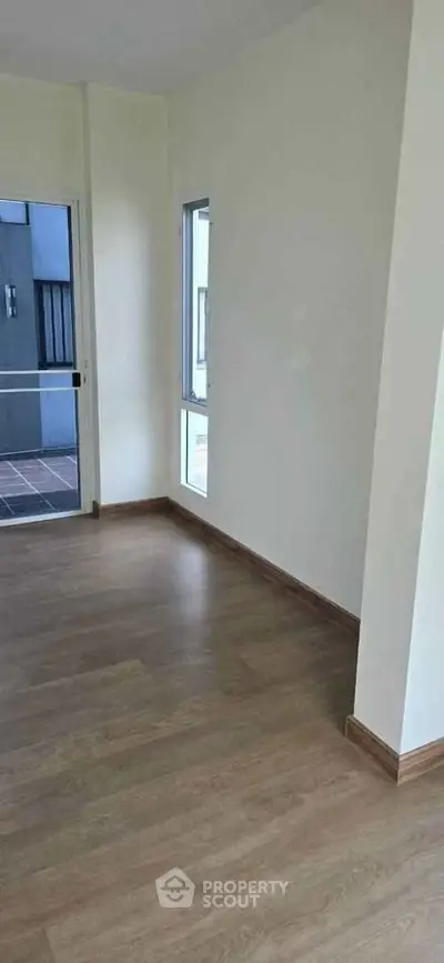 Spacious empty room with wooden flooring and large windows in modern apartment.