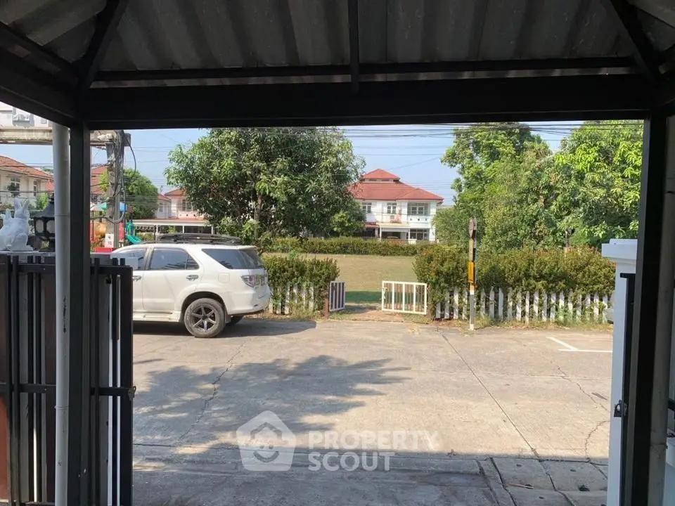Charming suburban view from a covered parking area with a white SUV and lush greenery.