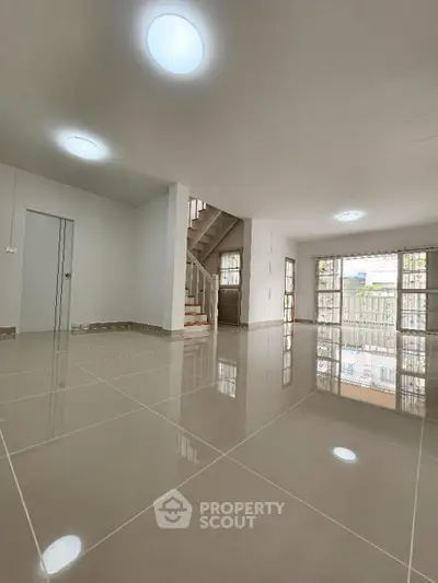 Spacious and bright living area with glossy tiled flooring, modern recessed lighting, and an elegant staircase leading to the upper level, perfect for luxurious living.