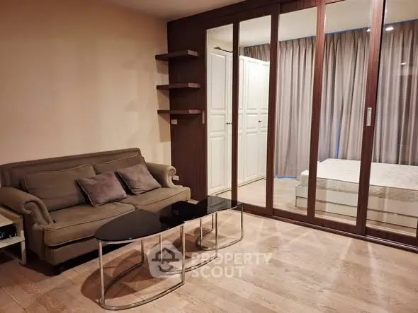 Modern living room with cozy sofa and glass coffee tables, adjacent to a stylish bedroom with sliding doors.
