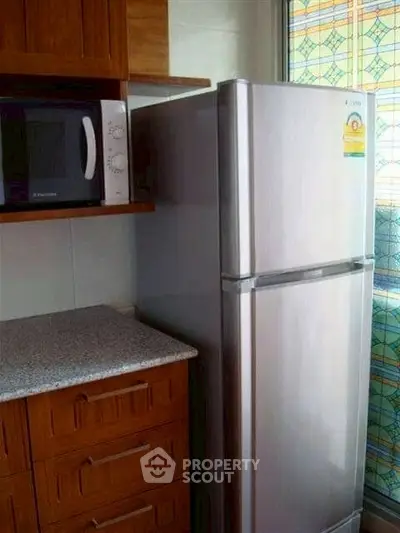 Modern kitchen with stainless steel fridge and microwave, featuring wooden cabinets and granite countertop.
