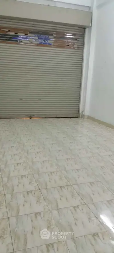 Spacious commercial space with tiled flooring and roller shutter door, ideal for retail or storage.