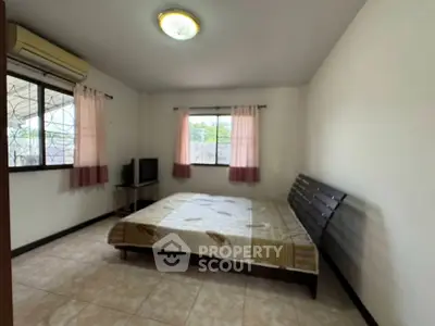 Spacious bedroom with large windows and natural light, featuring a cozy bed and air conditioning.