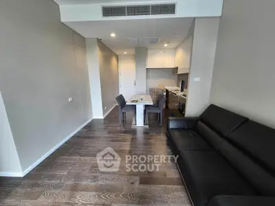 Modern living room with sleek black sofa and dining area in open layout apartment.