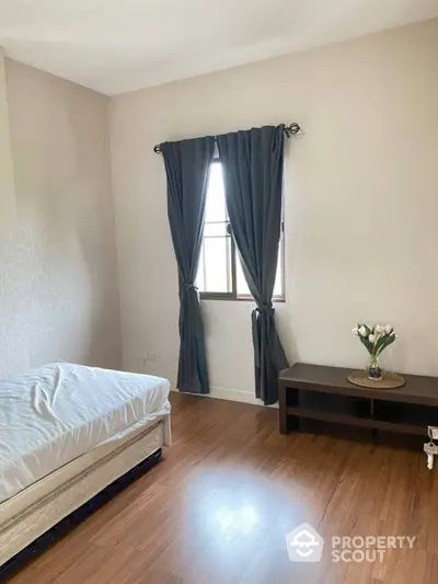 Spacious bedroom with polished hardwood floors, large window with elegant drapes, and minimalist decor for a serene living space.