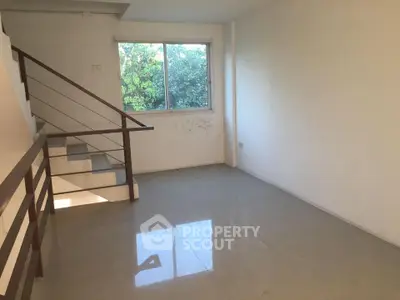 Spacious unfurnished room with staircase and large window overlooking greenery.
