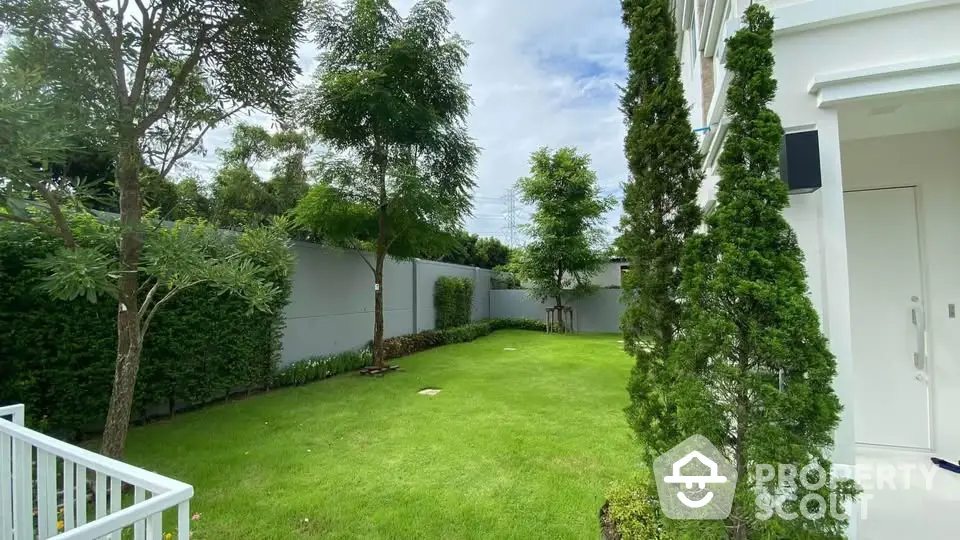 Spacious green garden with lush trees and modern white fence