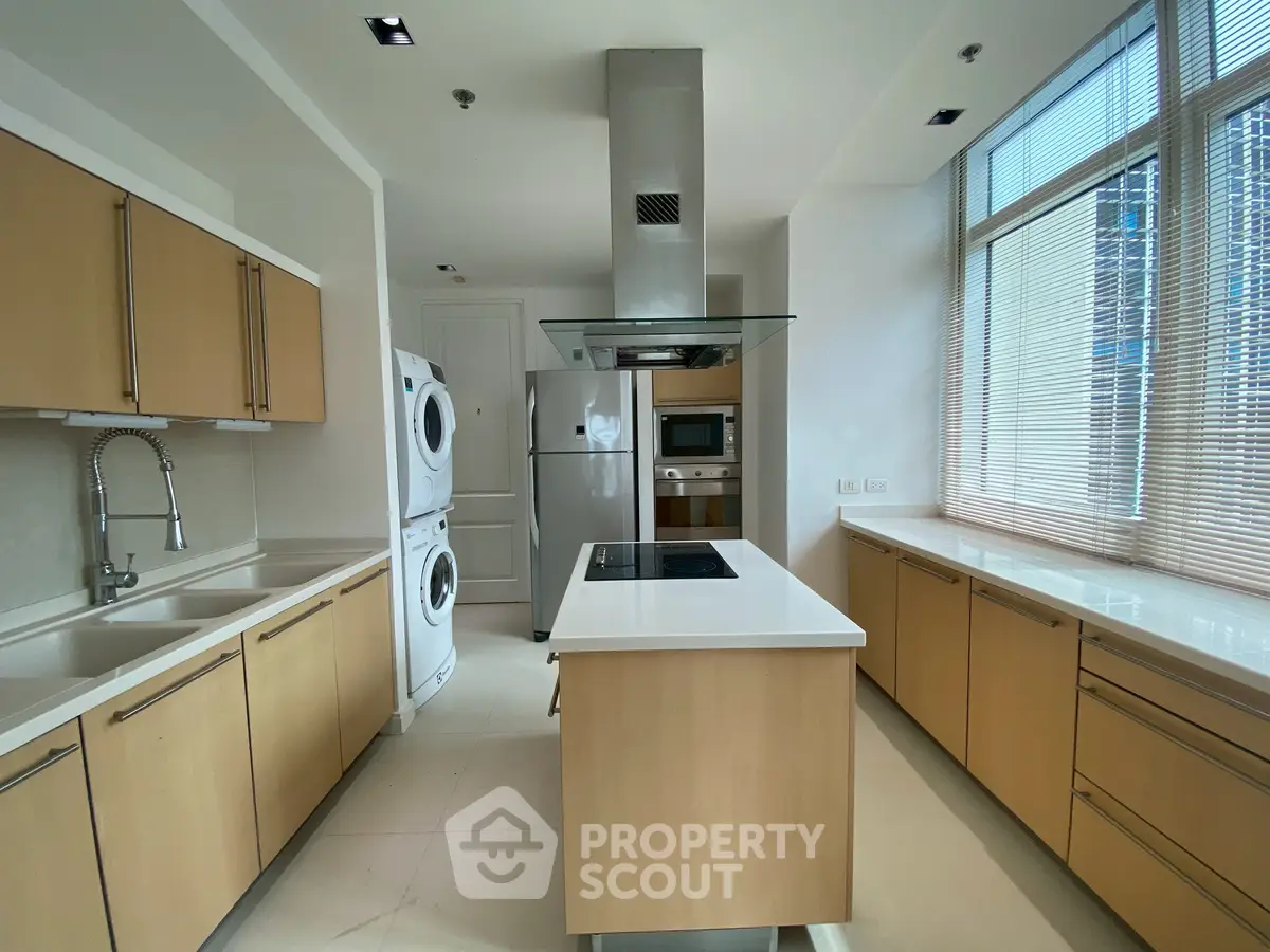 Modern kitchen with island, stacked washer-dryer, and stainless steel appliances in a bright, spacious layout.