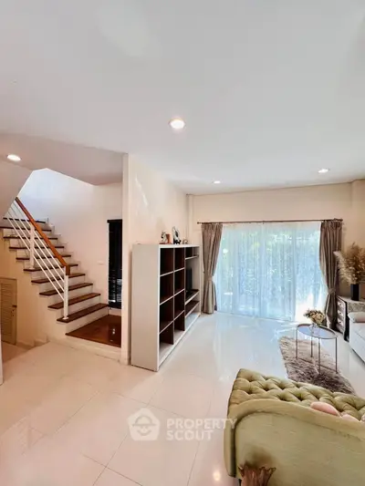 Spacious living room with elegant staircase and large windows for natural light