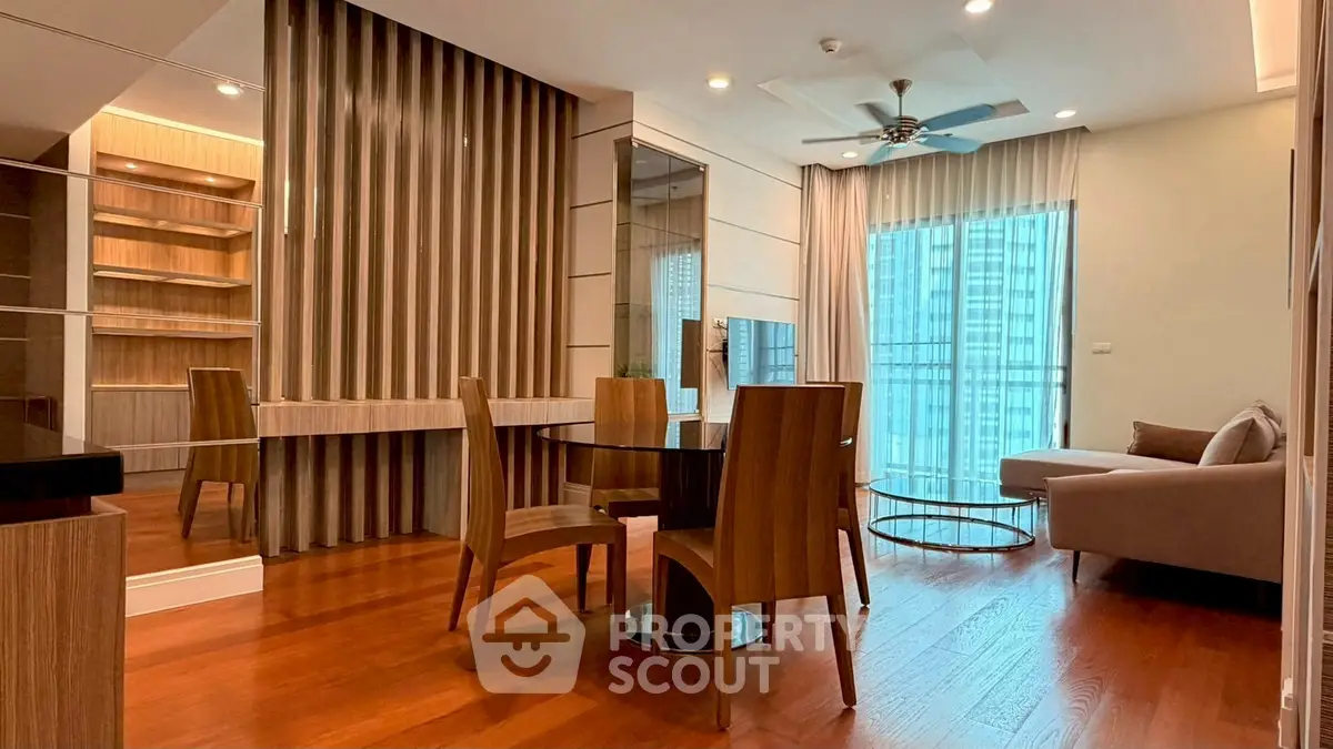 Modern living room with wooden flooring, stylish furniture, and large windows offering city views.