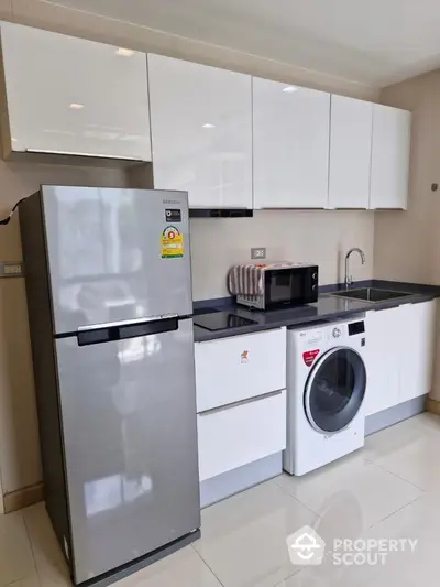 Modern kitchen with sleek white cabinets, stainless steel fridge, and washing machine