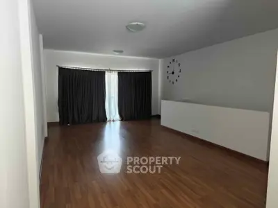 Spacious empty living room with wooden flooring and large window.