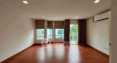 Spacious empty room with wooden flooring and large windows, ideal for customization.