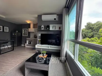 Modern living room with large window and stylish decor overlooking lush greenery.