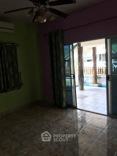 Spacious room with sliding glass doors leading to a poolside view, featuring tiled flooring and ceiling fan.