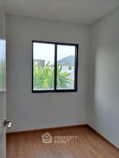 Bright empty room with wooden flooring and large window offering garden view.