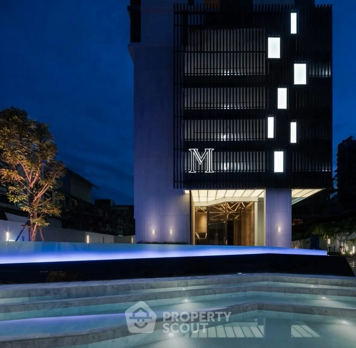Luxurious modern building entrance with illuminated facade and stylish pool at night.