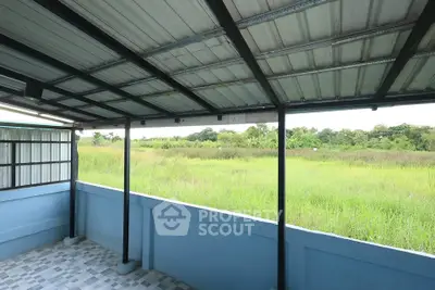 Spacious balcony with metal roof overlooking lush green fields, perfect for relaxation and outdoor enjoyment.