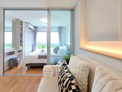 Modern bedroom with glass partition and cozy living area, featuring stylish decor and natural light.