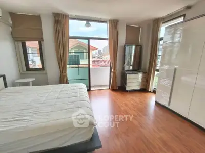 Spacious bedroom with large windows and balcony access, featuring modern furnishings and wooden flooring.