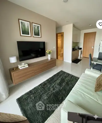 Modern living room with sleek furniture and wall-mounted TV, open layout to kitchen area.