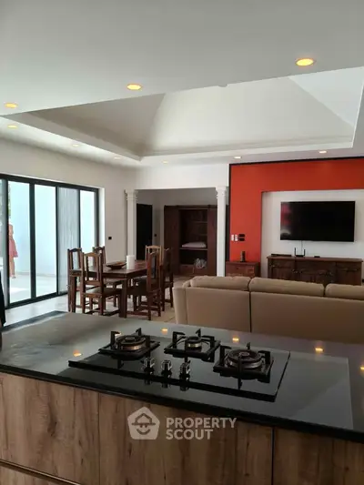Spacious open-plan living room with modern kitchen and elegant dining area, featuring a sleek gas stove and stylish decor.